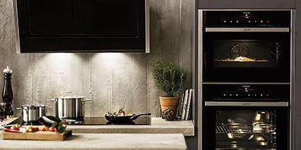 Modern kitchen with built-in double ovens, stainless steel pots, and fresh ingredients on countertop