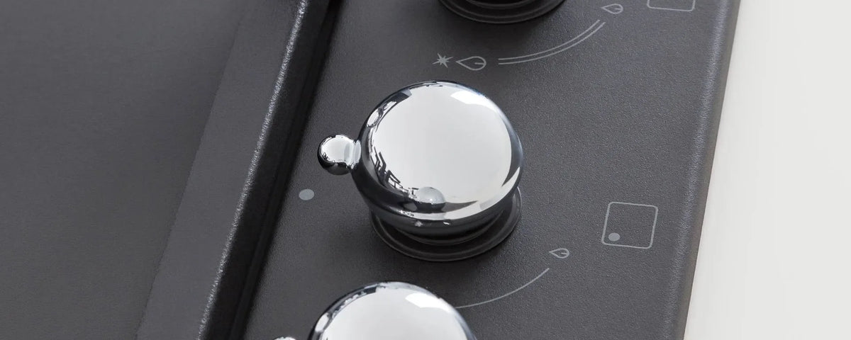 Close-up of a polished chrome control knob on a sleek black designer cooktop.