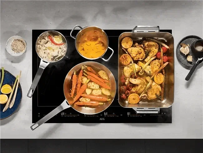 Falcon premium European Glass Black Upright 1100mm Induction Cooker with multiple pots and pans cooking assorted dishes on its sleek glass surface.