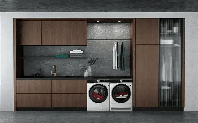 Modern laundry room with front load washer and dryer, wood cabinetry, and sleek gray tile backsplash