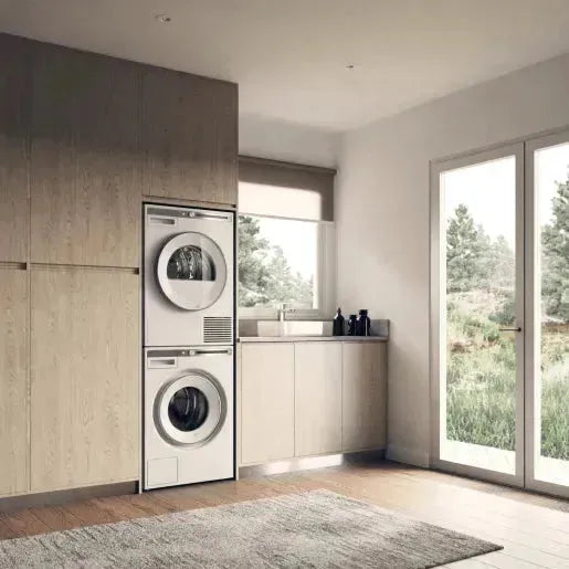 Stacked washer and dryer in modern laundry room with wood cabinets and large windows