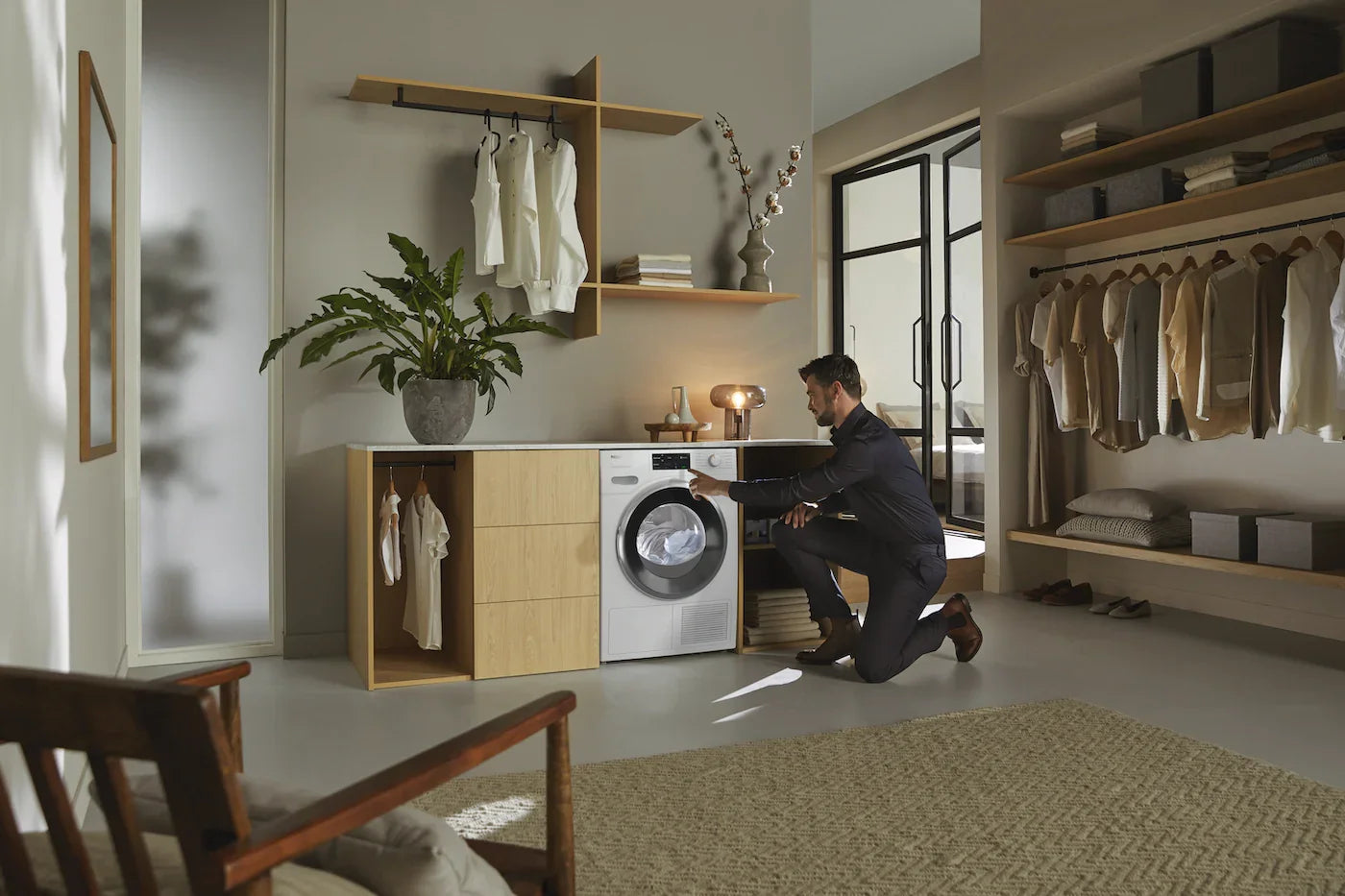 Man using modern front load washer in stylish laundry room with open closet and shelves