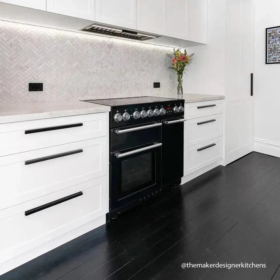 Black dual oven range in modern white kitchen with herringbone backsplash and dark hardwood floors
