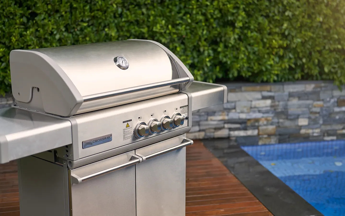 Stainless steel outdoor grill with side tables near poolside