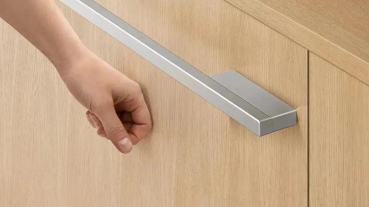 Modern stainless steel cabinet handle on light wood kitchen door, hand pulling open