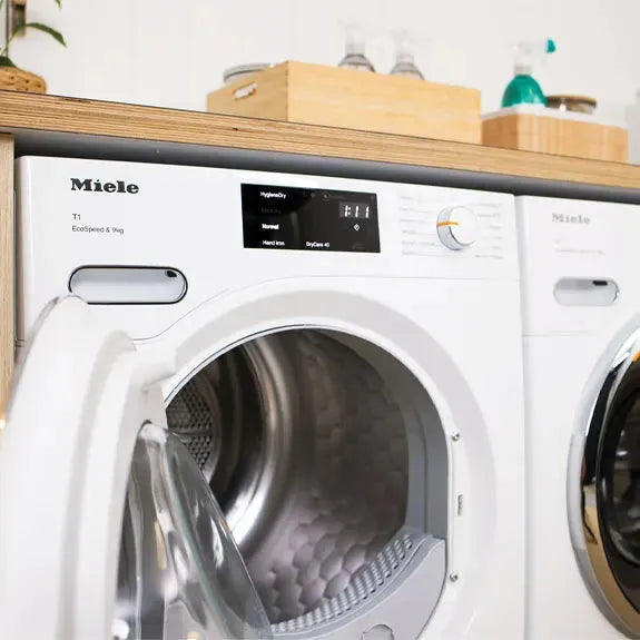 Miele front load washing machine with open door, sleek white design in modern laundry space