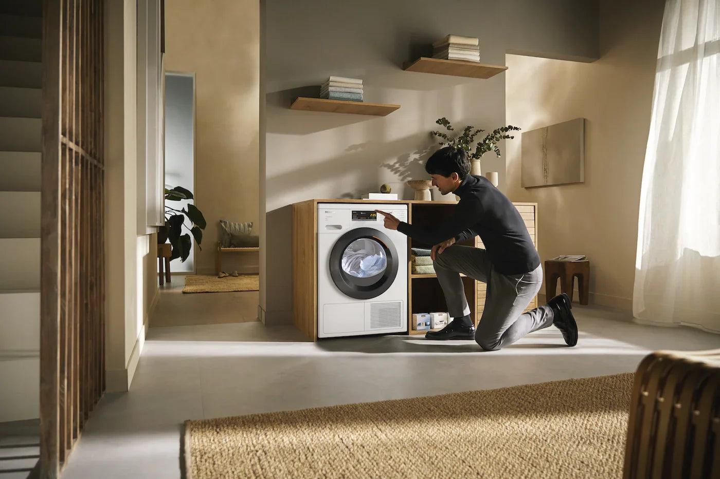Man adjusting settings on a modern front-load washing machine in a bright, minimalist laundry space.
