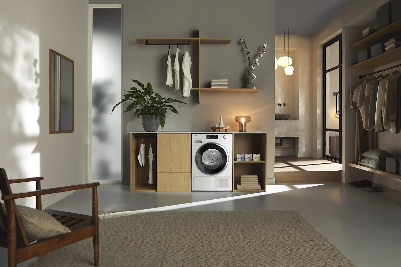 Modern laundry room with front load washing machine, wooden shelves, hanging clothes, and indoor plant