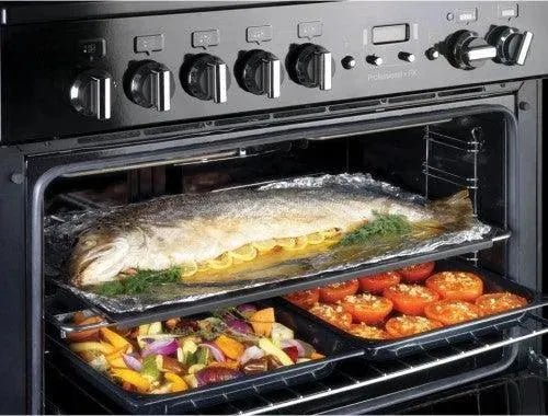 Black oven baking whole fish with lemon and roasted vegetables inside