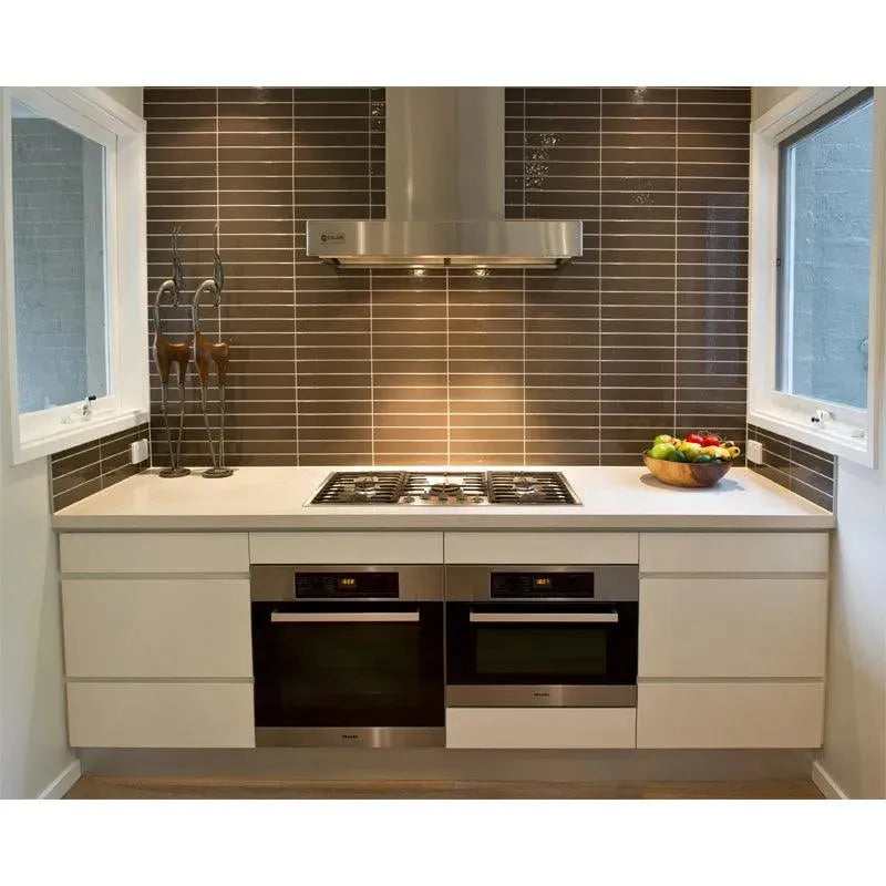 Modern kitchen with stainless steel gas cooktop, double ovens, and sleek white cabinetry under brown tile backsplash